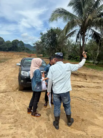 Perbincangan di tapak kerja tanah yang baharu diteroka, seorang memegang pelan sambil menunjuk ke arah tapak.